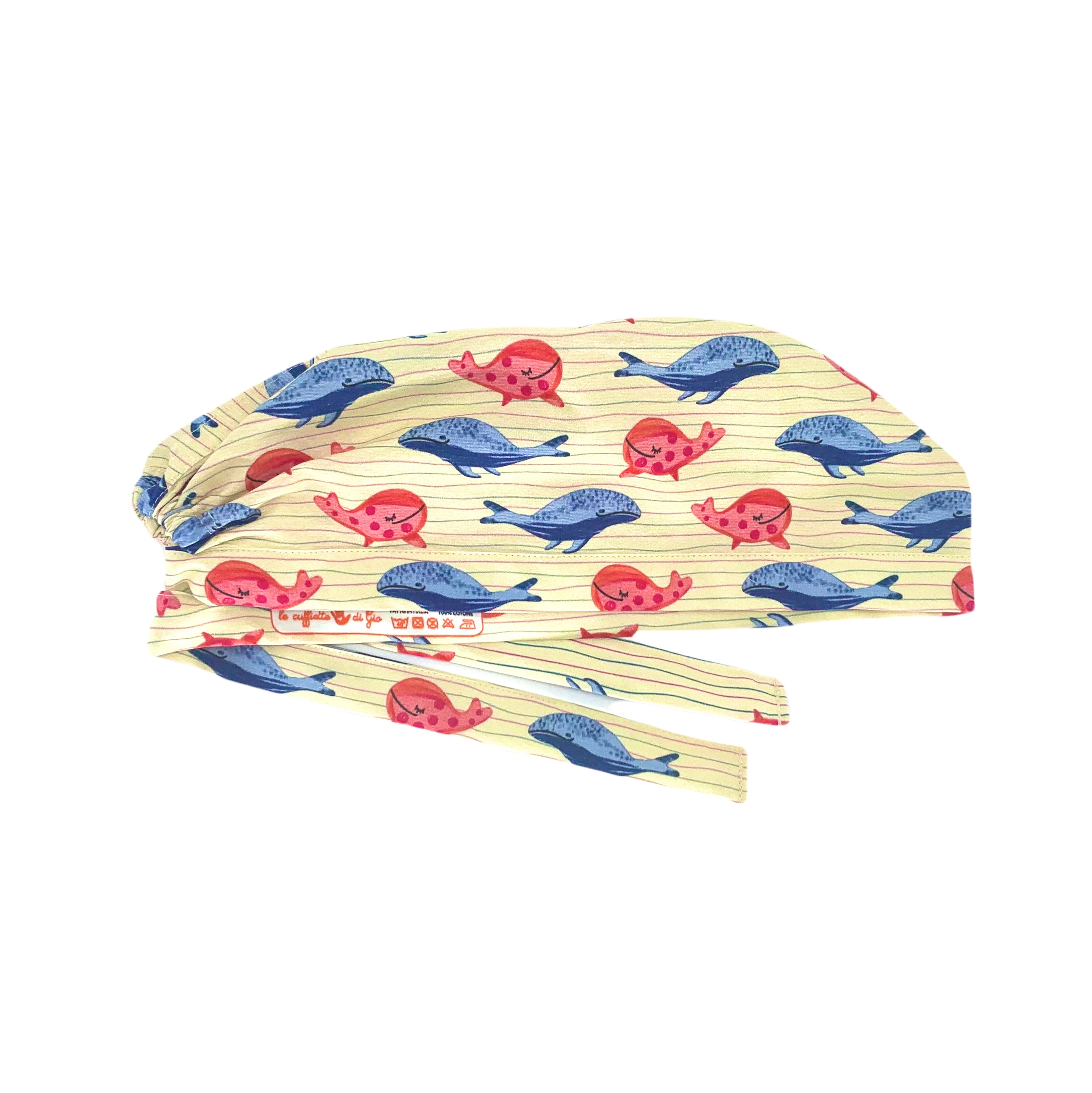 Cuffietta chirurgica con graziose balene blu e rosa sguazzano felici su sottili righe in tinta, sfondo beige.