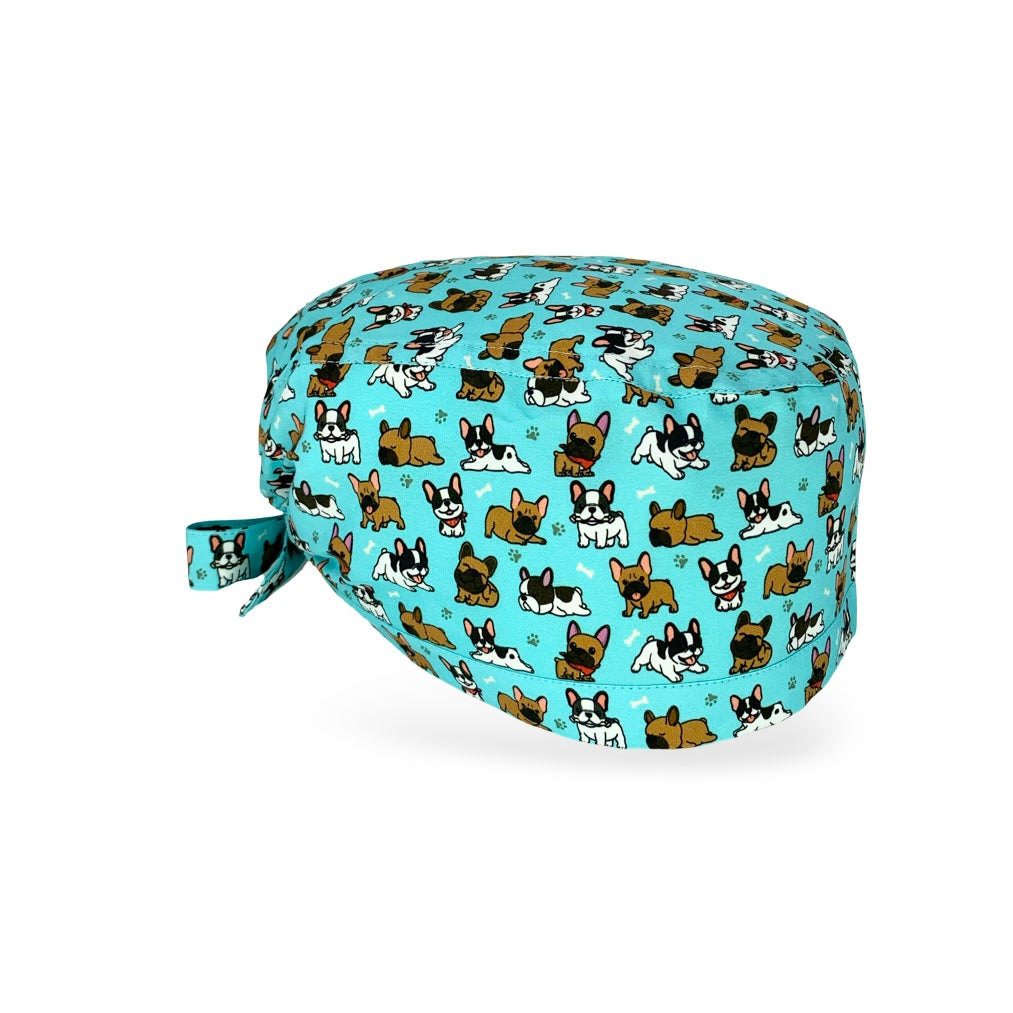 Una cuffietta chirurgica dedicata a una razza canina molto amata, il bulldog francese, qui rappresentata su sfondo azzurro intenso con diversi cagnolini in posizioni buffe, nella versione marrone e nero-bianco, alternati a zampette e piccoli ossi: semplicemente adorabile!