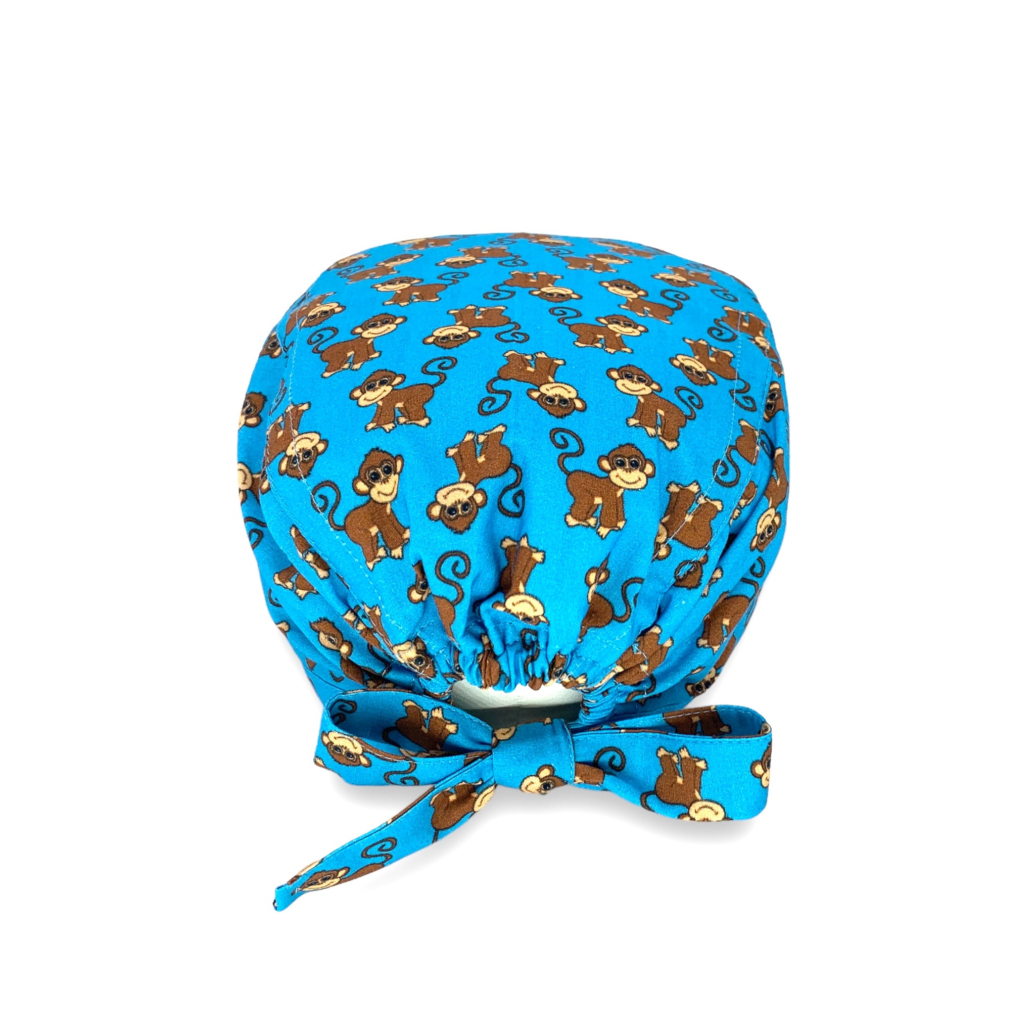 Cuffietta chirurgica con simpatiche scimmiette marroni, sorridenti e con la coda lunga arricciata, alternate a testa in giù o diritte; sfondo azzurro intenso