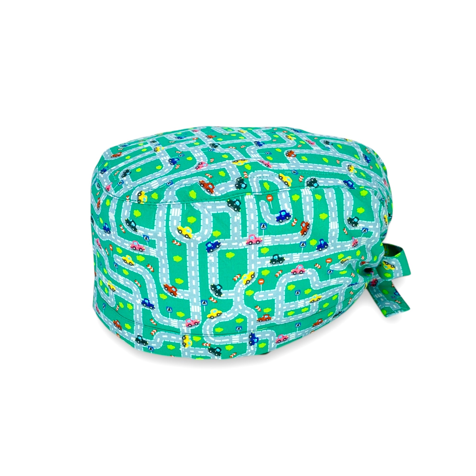 Una cuffietta chirurgica con piccole macchinine colorate in labirinti autostradali con semafori, strisce pedonali ed alberi verdi, su fondo verde.