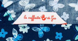 La base blu di questa cuffietta chirurgica esalta le sfumature di azzurro, turchese e verde acqua che colorano le ali di piccole farfalle e i petali di delicati fiorellini. 