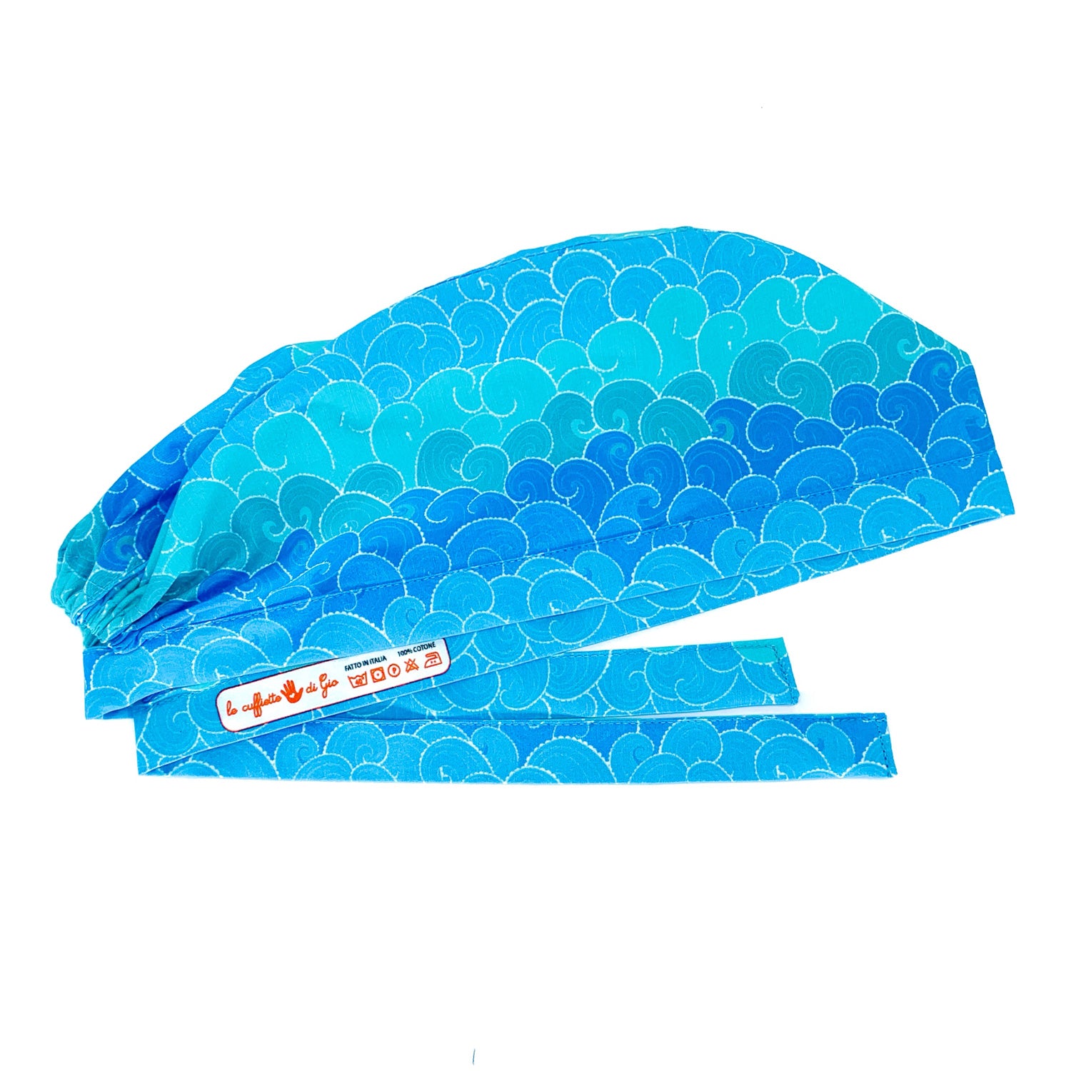 Foto laterale appiattita come se stirata di cuffia chirurgica con disegnate le onde del mare stilizzate in varie sfumature di azzurro. Laccio con logo interno le cuffiette di gio