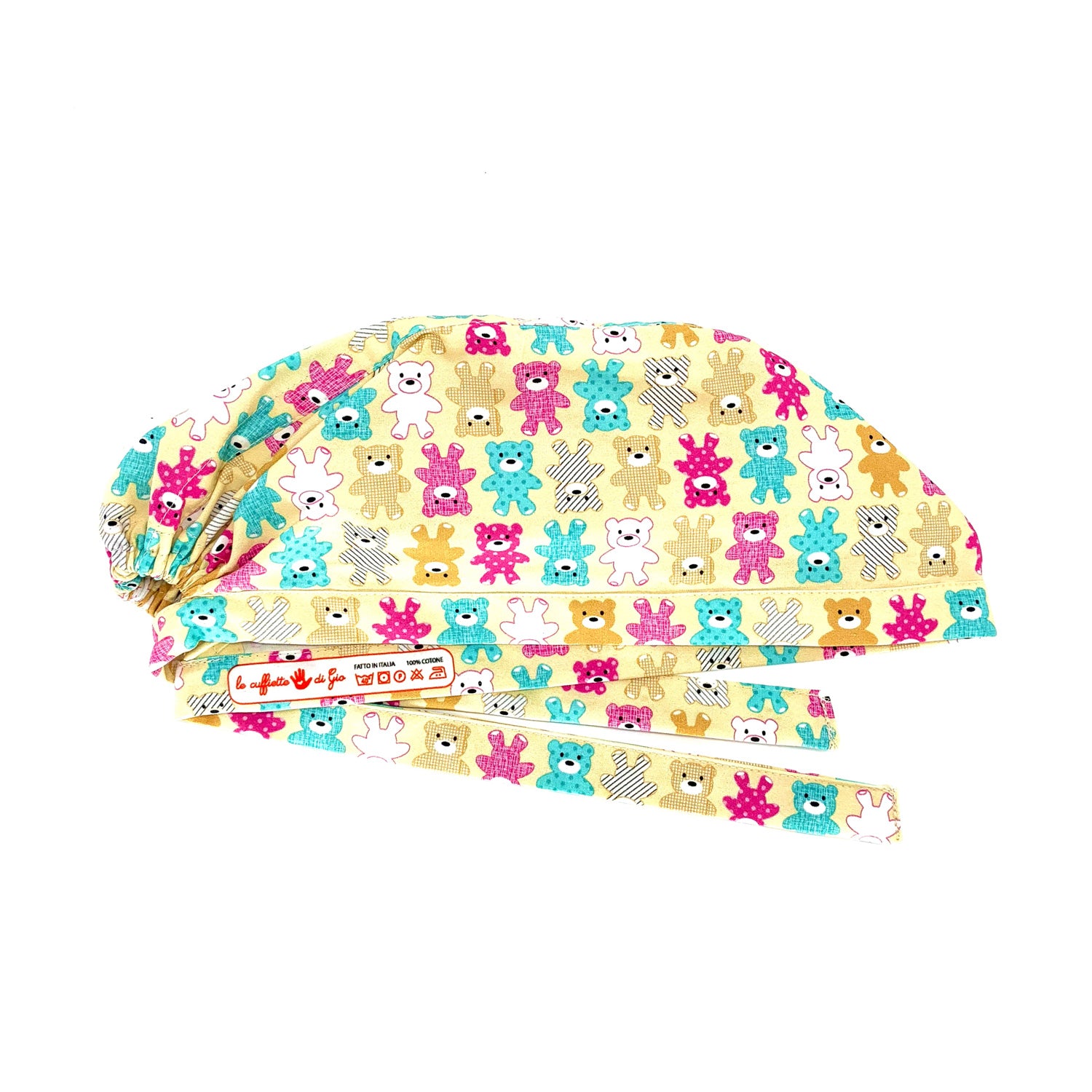 Foto laterale stirata di cuffietta chirurgica con stampa etichetta, le cuffiette di gio, su laccio interno, , con disegnati orsetti di peluche di vari colori tra cui fucsia, azzurro, bainco e marrone chiaro, Foto laterale cuffietta chirurgica con disegnati orsetti di peluche di vari colori su sfondo beige