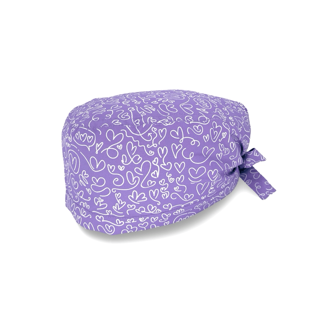 Un'elegantissima fantasia per questa cuffietta chirurgica, tappezzata di cuoricini scarabocchiati a mano con un tratto bianco su base tinta unita lilla, fucsia o turchese.