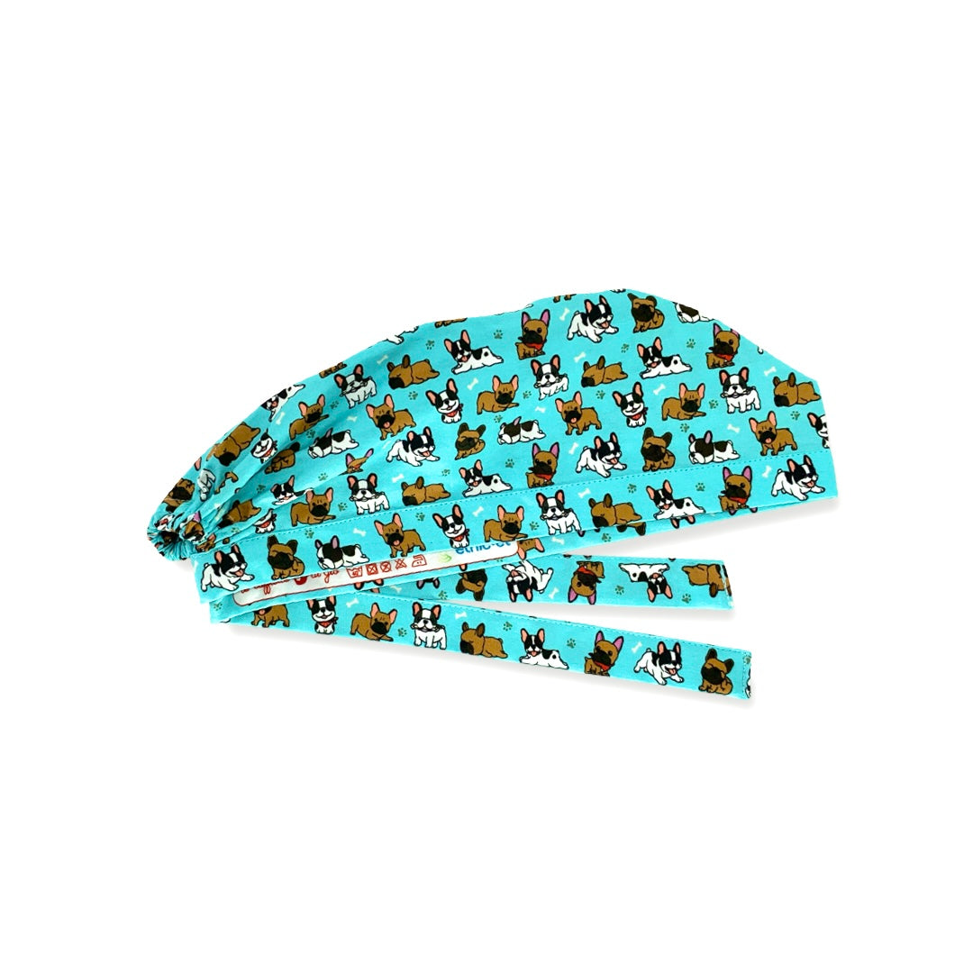 Una cuffietta chirurgica dedicata a una razza canina molto amata, il bulldog francese, qui rappresentata su sfondo azzurro intenso con diversi cagnolini in posizioni buffe, nella versione marrone e nero-bianco, alternati a zampette e piccoli ossi: semplicemente adorabile!