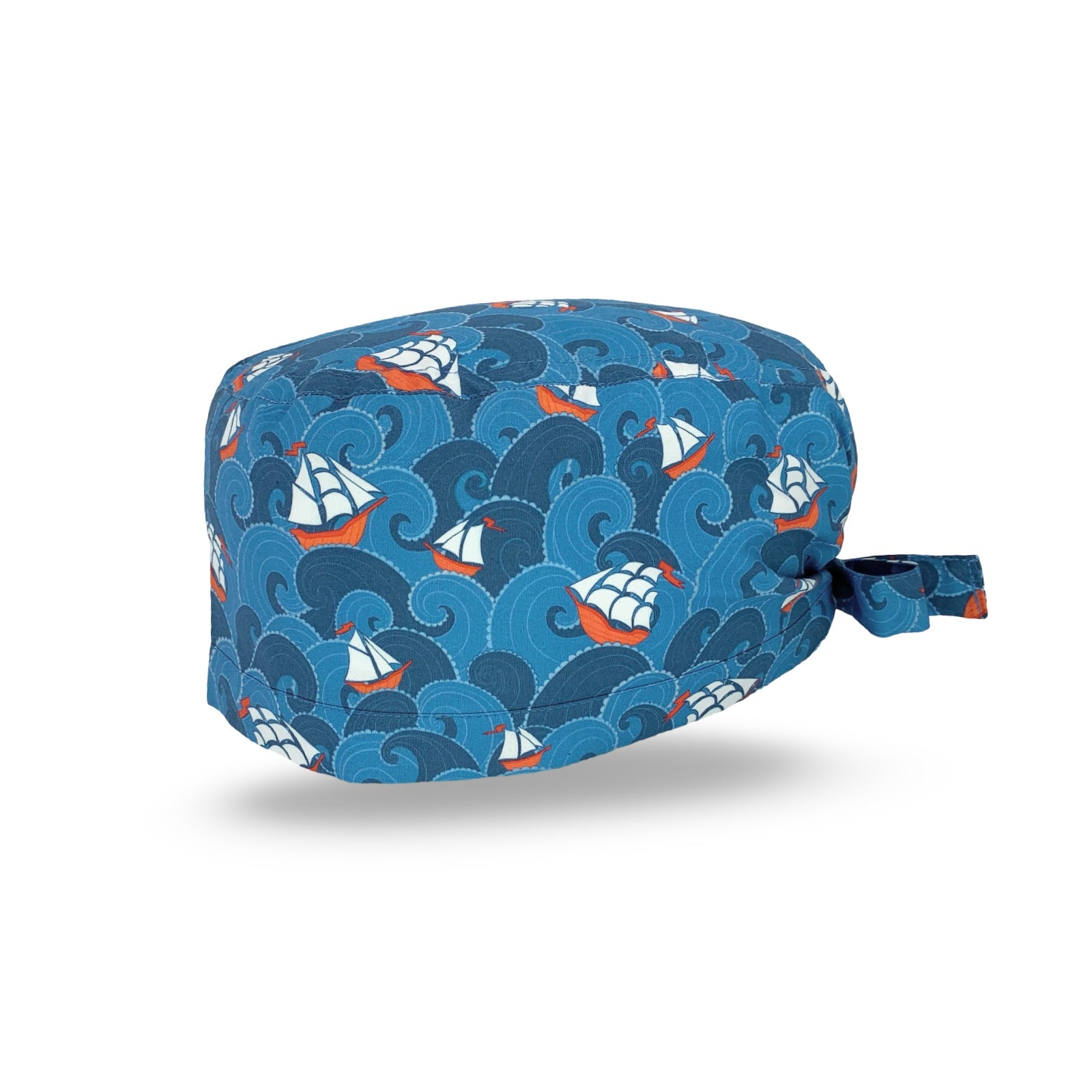Una cuffietta chirurgica a tema marino, con onde e velieri stilizzati; il tutto declinato in modo eleganti nei toni dell'azzurro e blu medio, con un tocco di rosso e bianco.